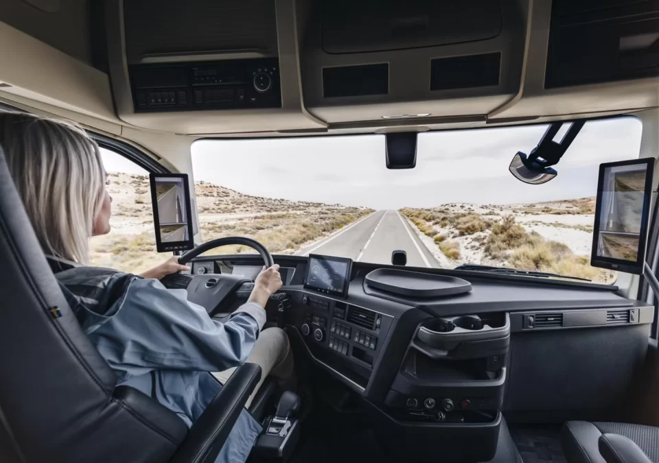 Motorista mulher conduzindo caminhão Volvo equipado com tecnologia antissono e de detecção de desatenção, que utiliza câmeras para identificar sinais de fadiga e aumentar a segurança nas estradas